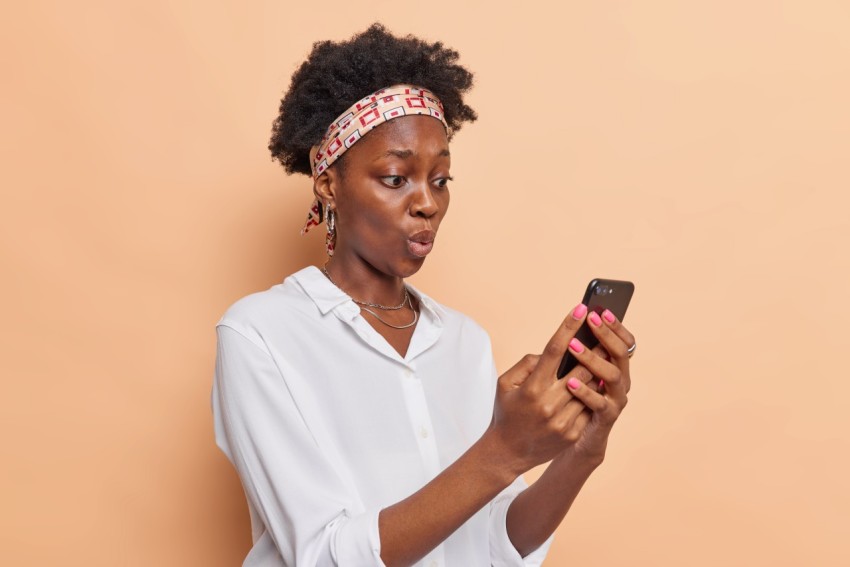 Emotive surprised woman stares at smartphone screen has shocked